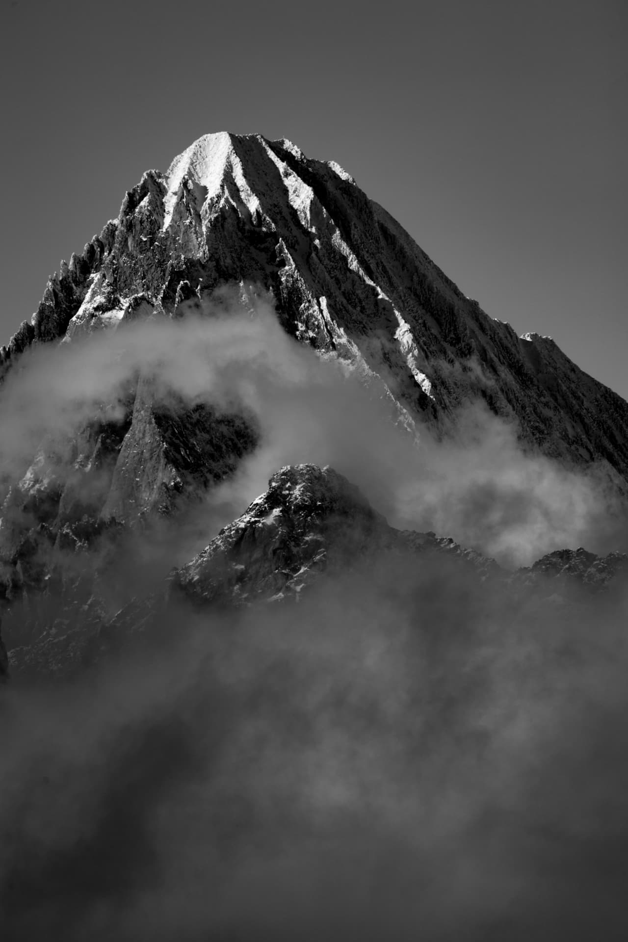 Schwarzweisse Hochformat-Silhouette eines Gipfels in wirbelnden Wolken